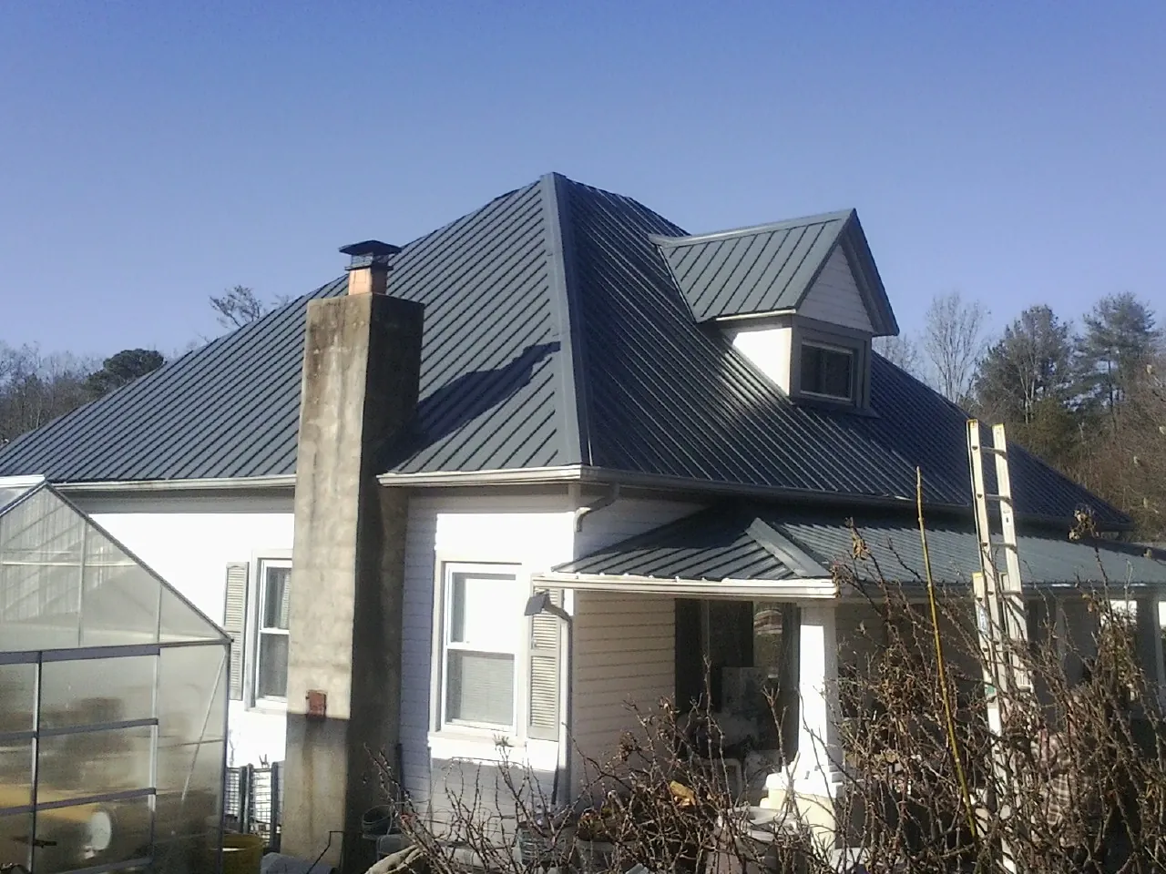 Dark blue standing seam metal roof on a white farmhouse with dormer — Slate & Tile Roof Repair by Roofing Brothers in Conetoe