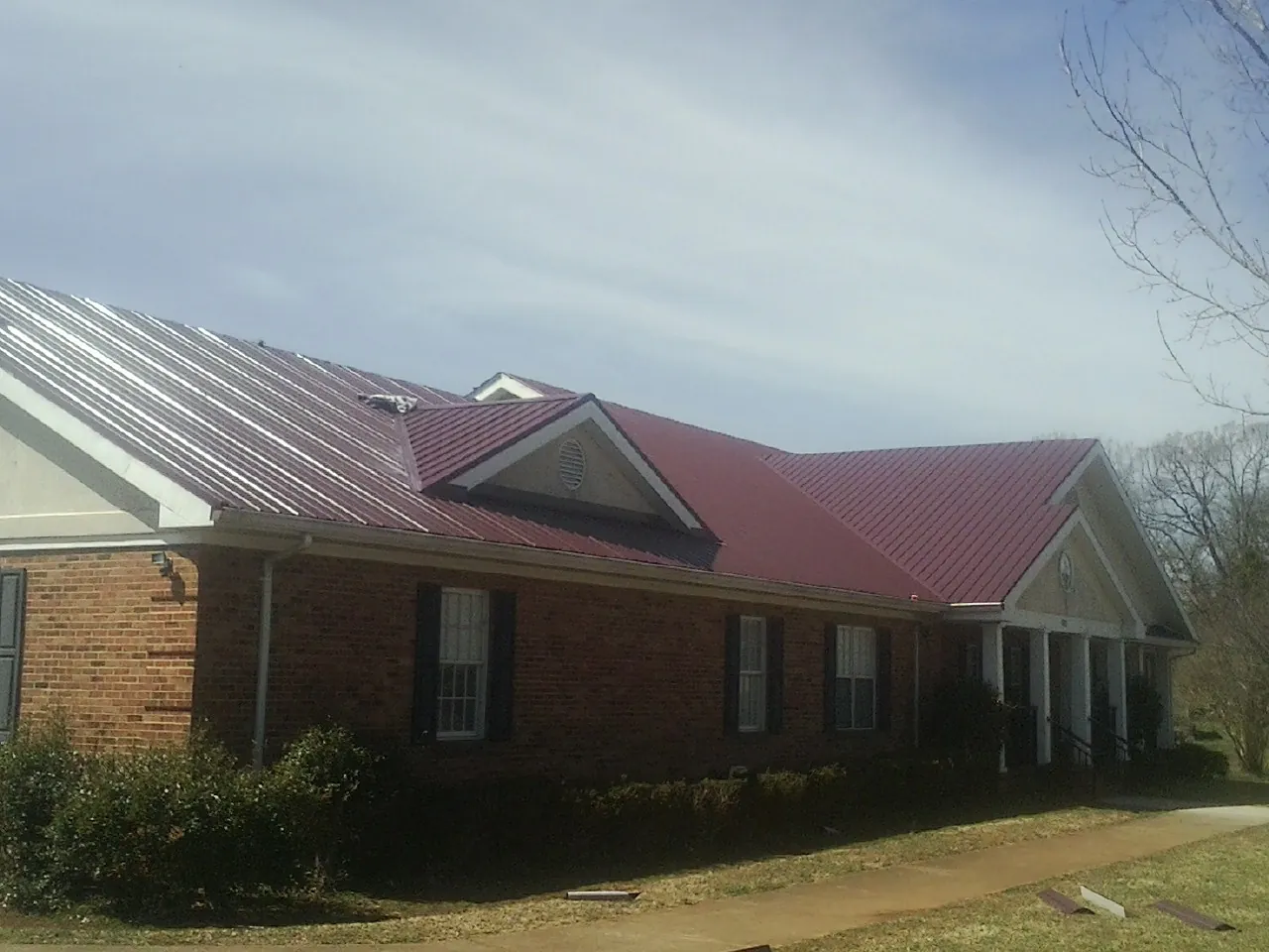 Red metal roof with gabled entries on a long brick building, from a Hail Damage Roof Repair job in Conetoe