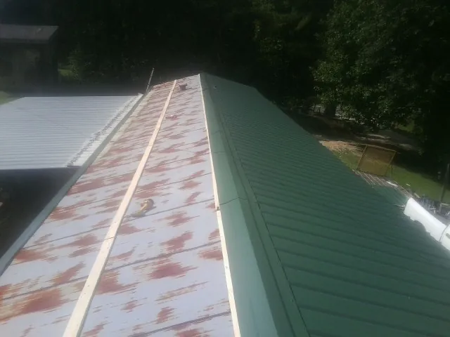 Old rusted panels beside newly installed green metal roofing — Wind Damage Roof Repair by Roofing Brothers in Conetoe