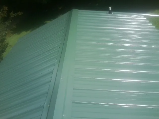 New green metal panels meeting at the ridge of a roof — Flat Roof Repair work by our crew in Conetoe