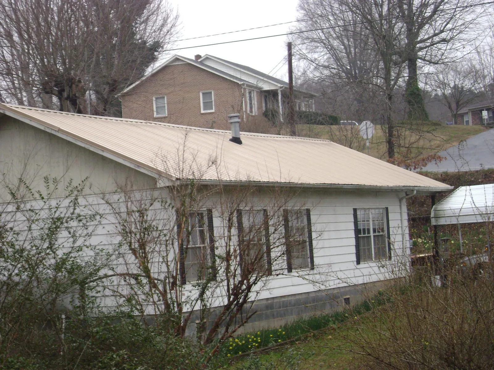 Tan metal roof on a white sided house set into a hillside — Commercial Roofing by Roofing Brothers in Conetoe